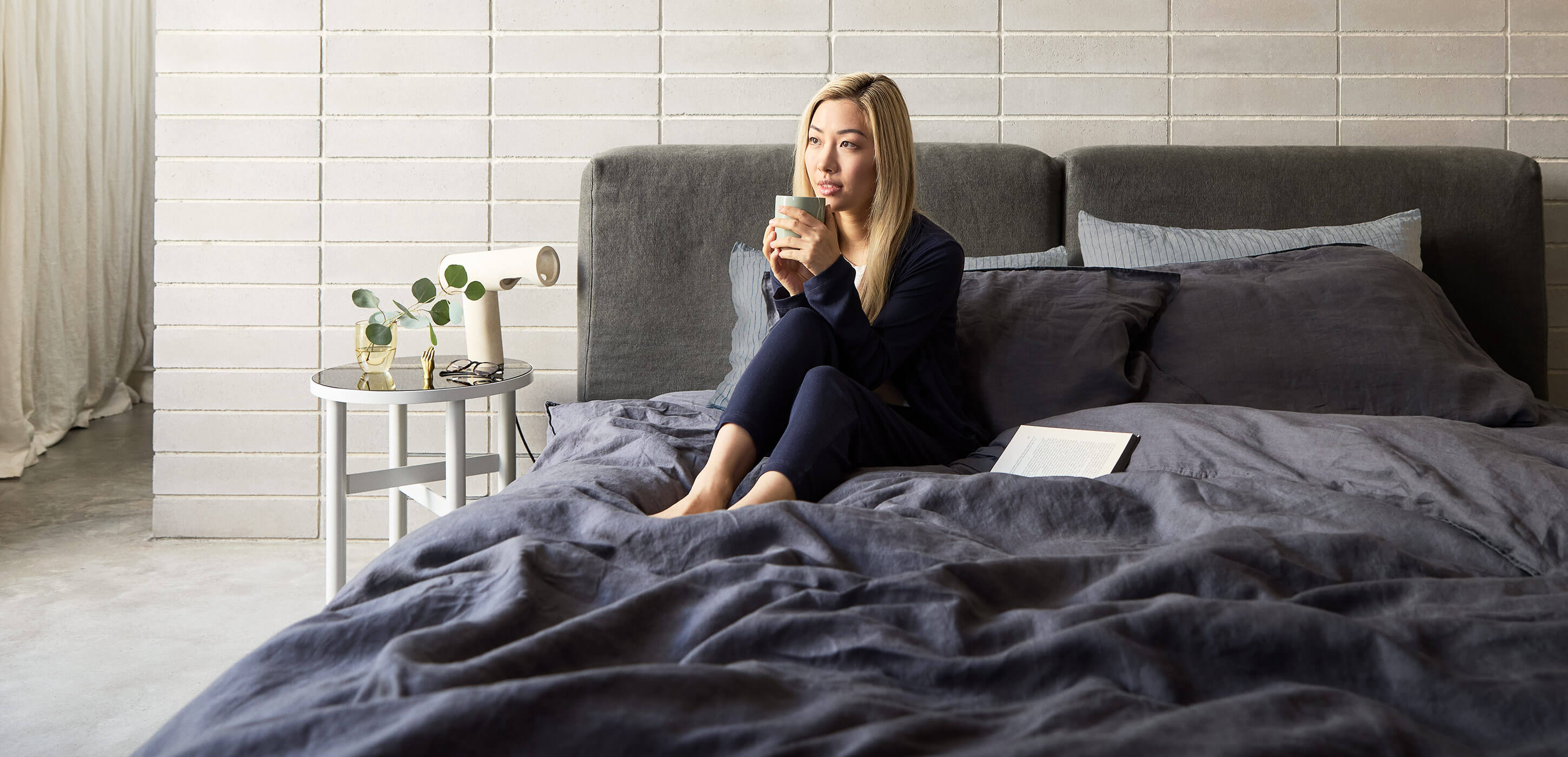 a woman sitting on a bed with a hot drink